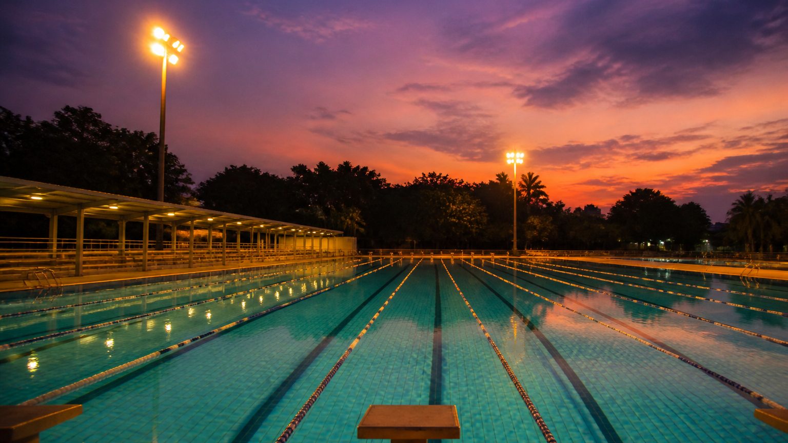 Outdoor pool at dusk with floodlights on the water and a starting block in the foreground