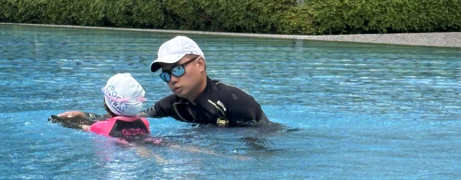 A coach in the water guiding a young swimmer through a lesson at an outdoor pool